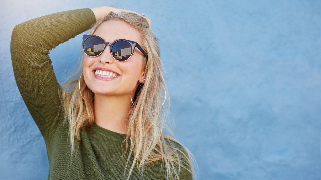 woman wearing sunglasses looking toward the sun and smiling confidently