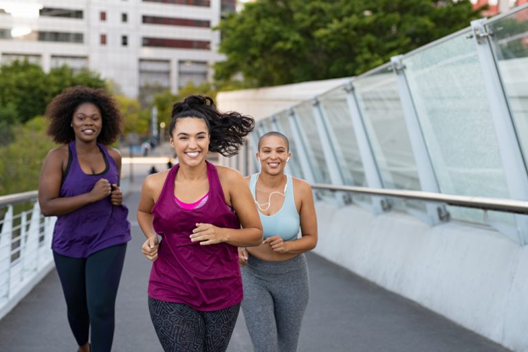 Three women jogging on a city bridge together.
