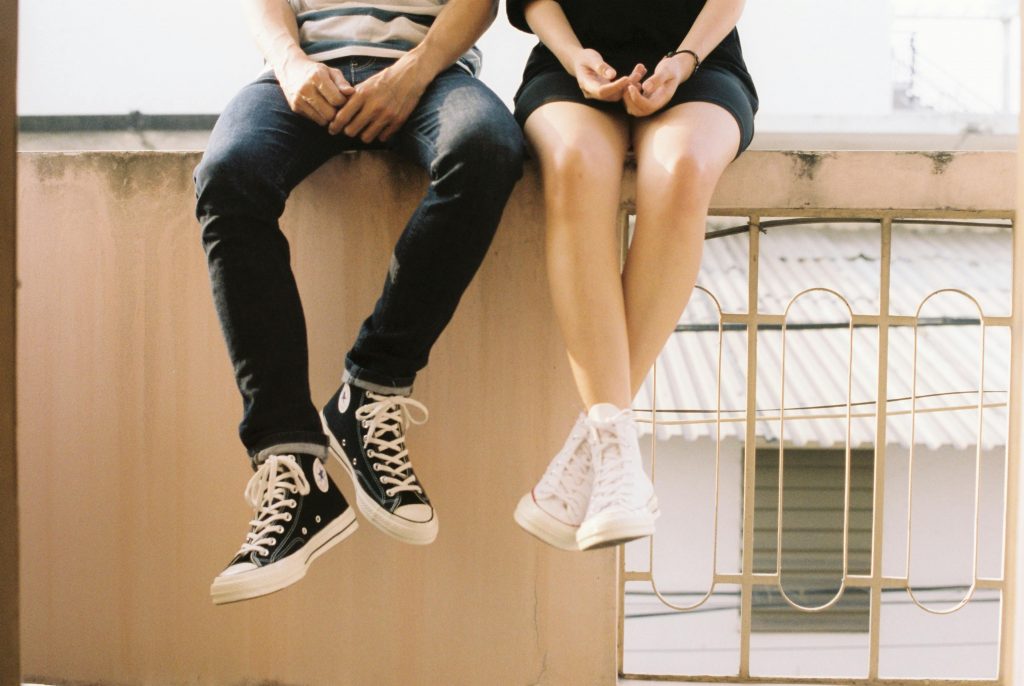 couple wearing sneakers, sitting on a balcony railing