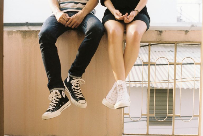 couple wearing sneakers, sitting on a balcony railing