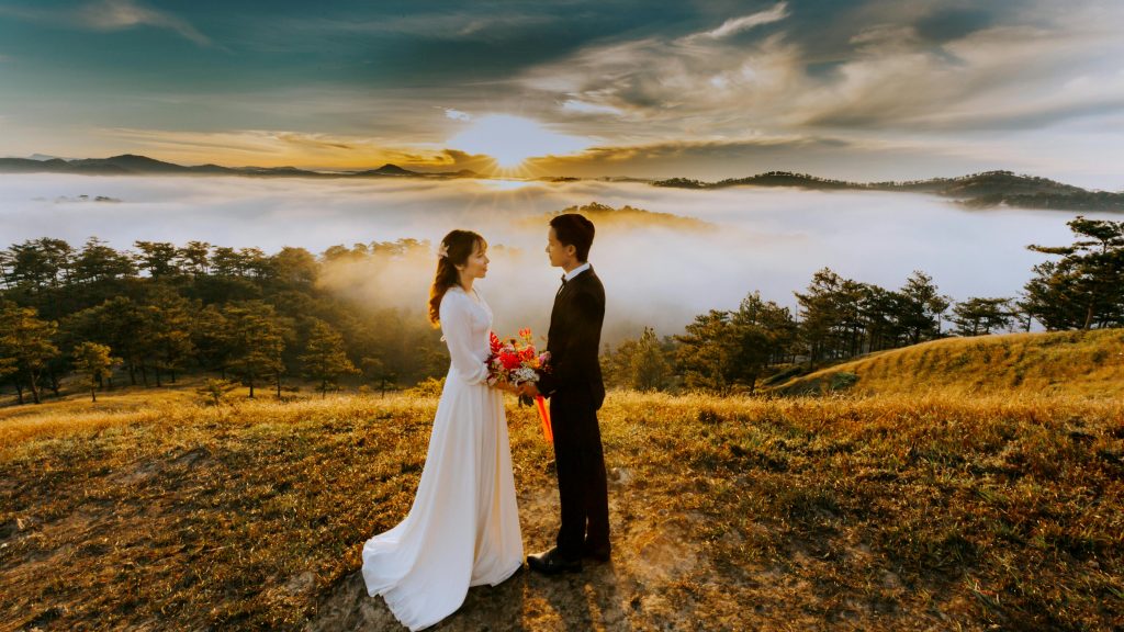 newlyweds standing on a hill overlooking a sea of clouds and a sunset